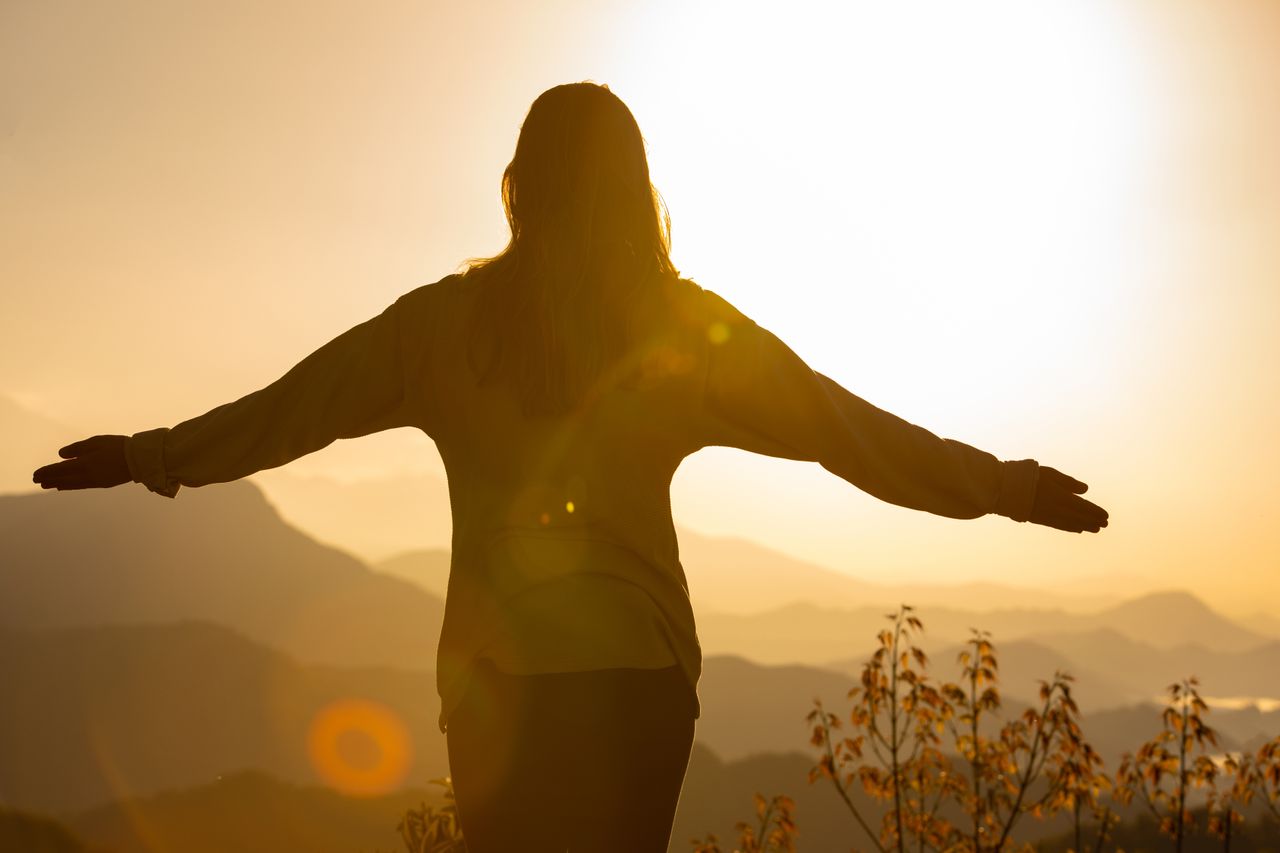 Crafting Captivating Headlines: Your awesome post title goes here A woman stands with arms open, embracing the sunrise in a mountainous landscape, creating a tranquil silhouette.