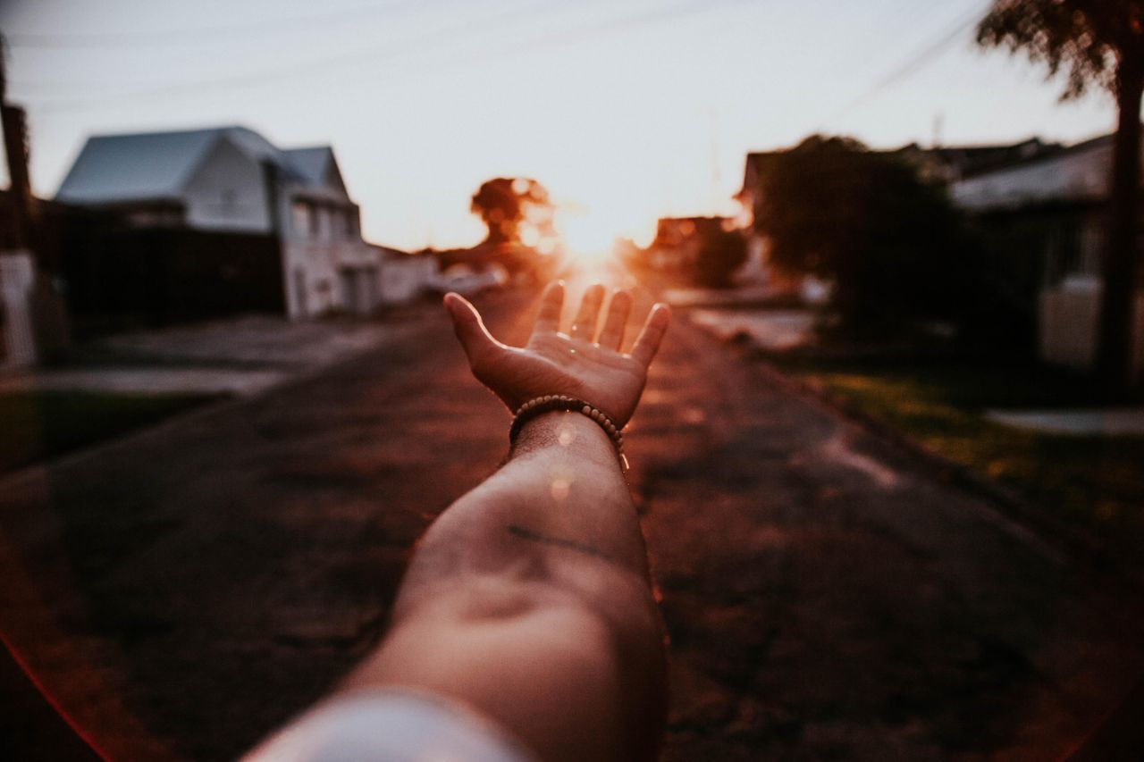 Dramatic view of a hand reaching towards a sunset on a quiet urban street.